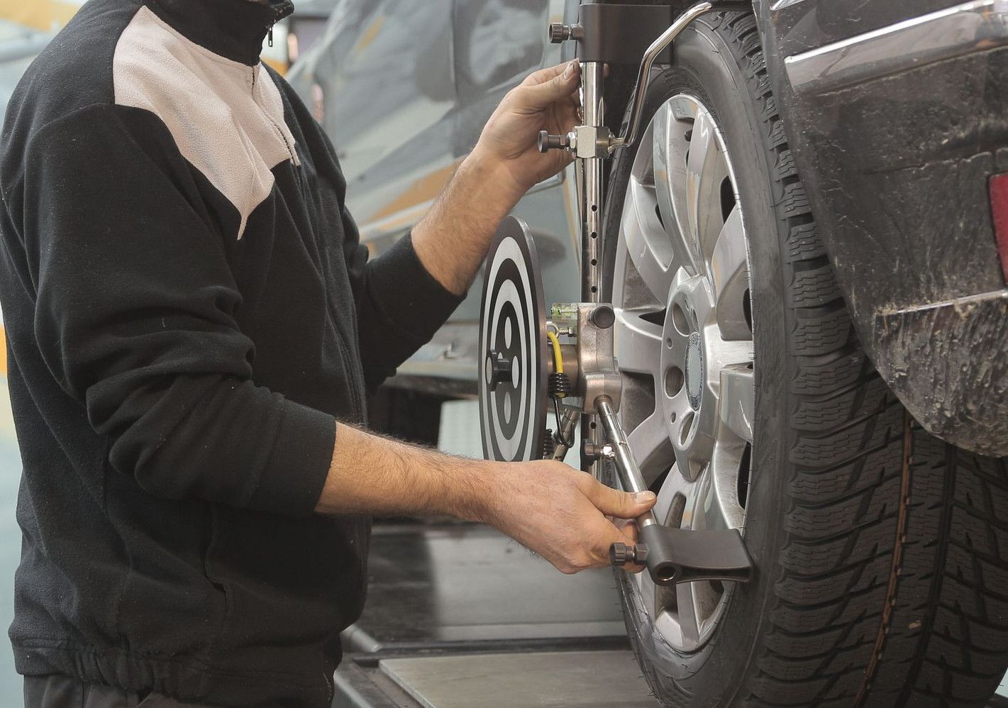 Mechanic performing wheel alignment on a car in a professional garage setting.